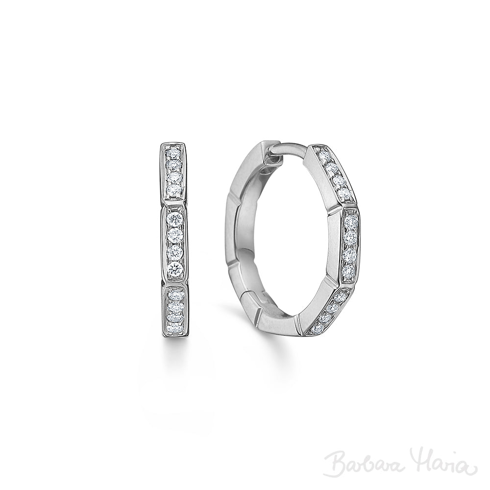 Devoted øreringene er fremstillet i 14 karat blankt og rhodineret hvidguld med brillanter hele vejen rundt på øreringen, i alt 0,15 ct. TW/VS. Øreringene er designet af Maria Nielsen, Guldsmed Barbara Maria